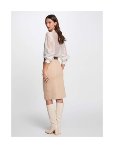 Mulher com blusa branca, saia bege e botas bege num fundo branco