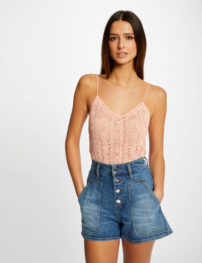 Mulher com top cor de rosa e calções de ganga azuis diante de fundo branco