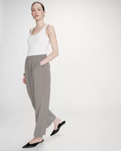 Mulher vestindo blusa branca, calças cinzentas e sapatos pretos em fundo branco