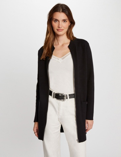 Mulher com casaco preto, top branco e calças brancas, fundo branco