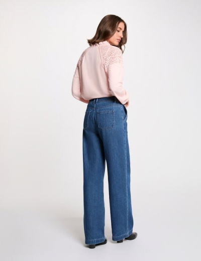 Mulher de costas com calças de ganga azuis largas e blusa rosa clara com detalhes rendados nos ombros