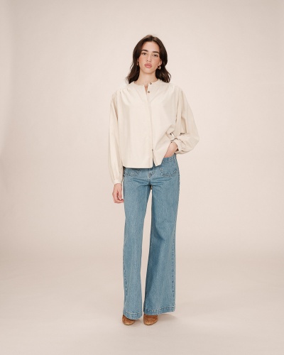 Mulher a vestir blusa creme de mangas bufantes e jeans azul claro largo