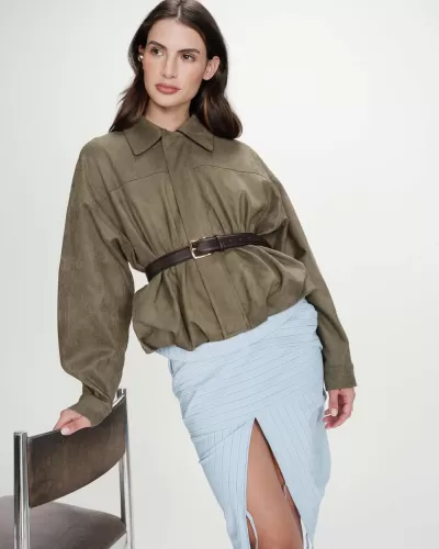 Mulher com casaco verde-oliva, saia azul clara riscada, cinto castanho e cadeira