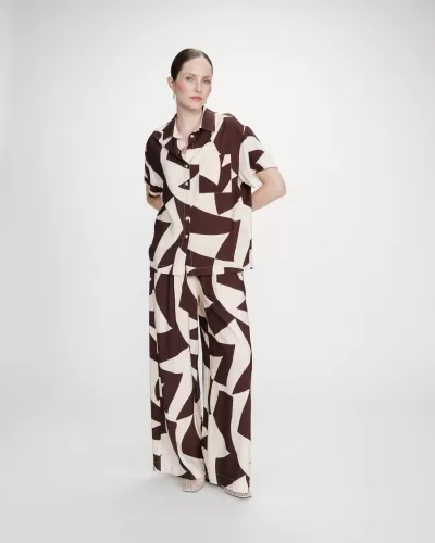 Mulher vestindo conjunto em padrão geométrico castanho e creme com camisa de manga curta e calças largas.