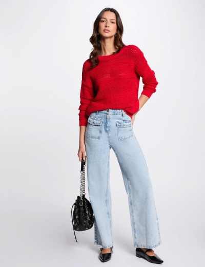 Mulher com suéter vermelho, jeans claros largos e bolsa preta com alça de corrente.