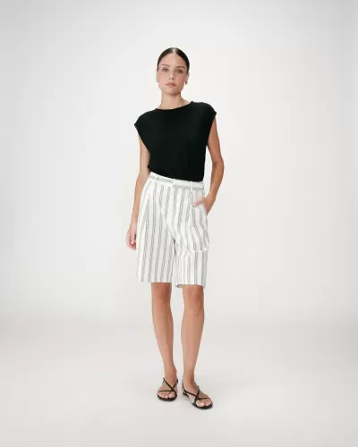 Mulher com top preto e calções brancos às riscas verticais pretas com sandálias pretas