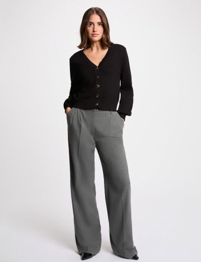 Mulher com cardigã preto e calças cinzentas num fundo branco