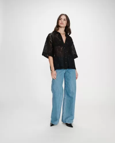 Pessoa com camisa preta transparente de renda e calças de ganga azul claras largas