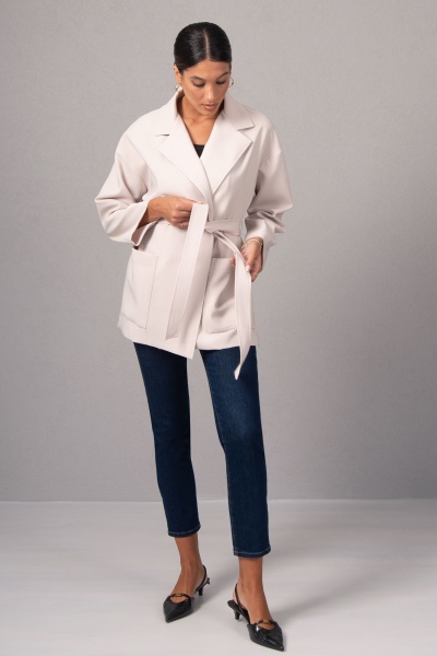 Casaco bege claro com cinto e gola de lapela usado por mulher com calças de ganga e sapatos pretos