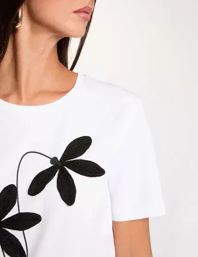 T-shirt branca com bordado preto de flor em fundo branco