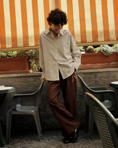 Pessoa com roupa casual numa esplanada com cadeiras de plástico e toldo às riscas laranja e bege