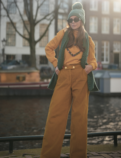 Mulher com roupa casual castanha e verde ao ar livre junto a canal.