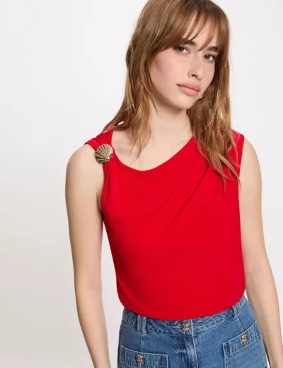 Blusa vermelha sem mangas com joaninha dourada no ombro e calças de ganga azul