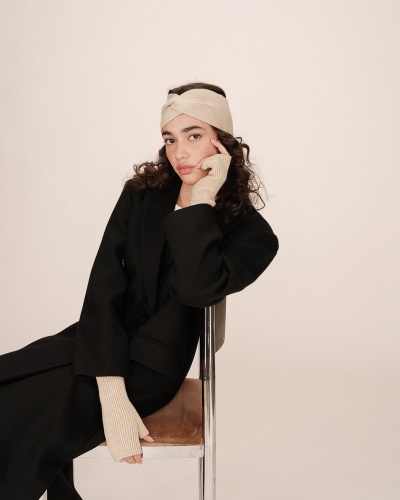 Mulher com casaco preto e acessórios bege de malha sentada numa cadeira