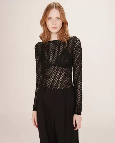 Blusa preta de renda com padrão geométrico e mangas compridas, vestida com calças pretas.