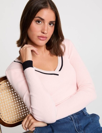 Mulher com camisola rosa clara de malha canelada com detalhes pretos sentada numa cadeira de madeira com assento em palhinha