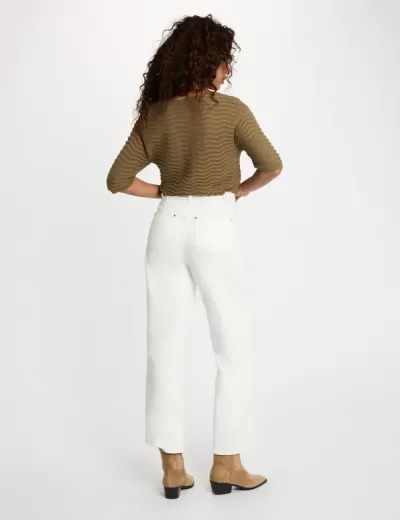 Mulher de costas com camisola castanha, calças brancas e botins camel.