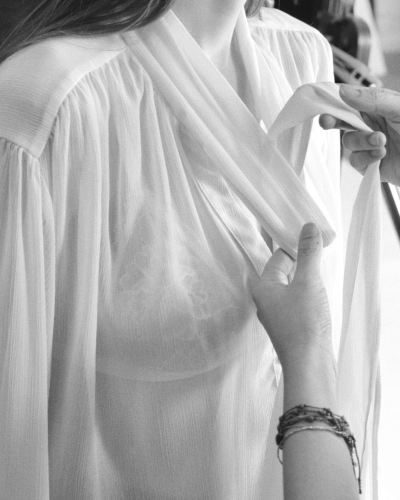 Blusa branca feminina transparente com detalhe franzido e mãos ajustando o decote