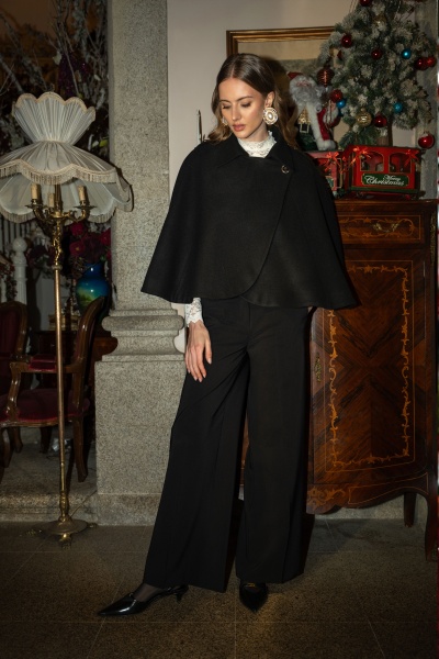 Mulher com capa preta e calças pretas num ambiente interior clássico com decoração de Natal