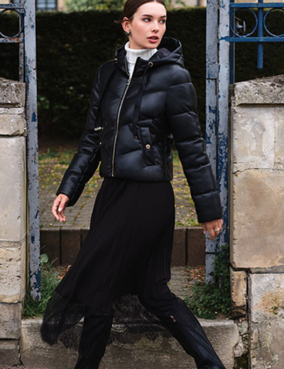 Mulher com casaco acolchoado preto e vestido preto num portão de ferro azul