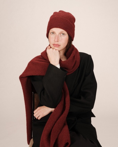 Mulher com gorro e cachecol de malha vermelho escuro e casaco preto sentada