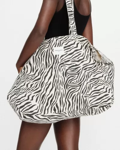 Mala grande estampada tipo zebra preto e branco com etiqueta Grace & Mila, usada ao ombro.