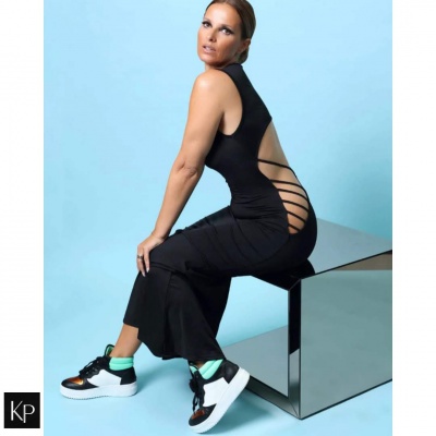 Mulher com vestido preto de recortes laterais e ténis brancos com detalhes a verde sentada em superfície espelhada