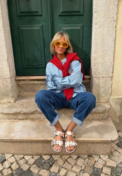 Mulher sentada em degraus de pedra com roupa casual e óculos amarelos grandes