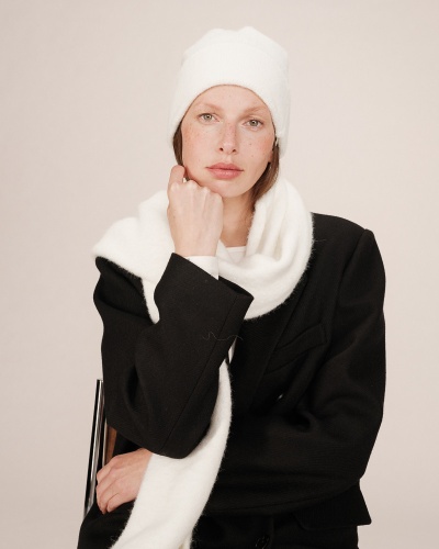 Mulher com gorro e cachecol brancos e casaco preto sentada