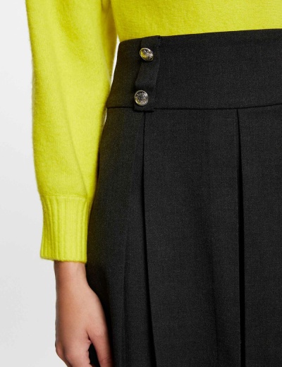 Vista parcial de saia preta plissada com botões prateados e camisola amarela