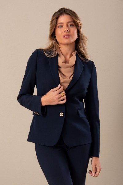 Mulher com blazer azul marinho e blusa bege clara em fundo bege