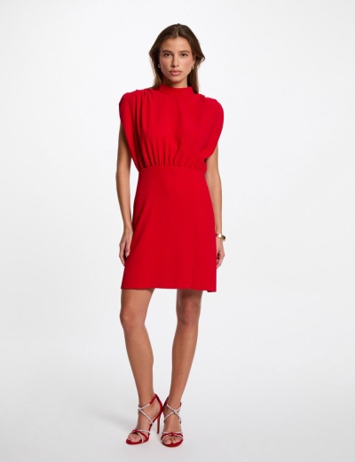 Modelo veste vestido vermelho curto com ombros almofadados e sandálias vermelhas.