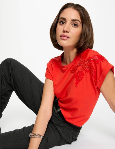 Mulher com t-shirt vermelha bordada e calças pretas sentada