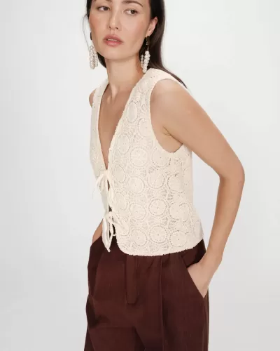 Blusa de crochet bege claro com padrões circulares e laços, usada com calças castanhas largas