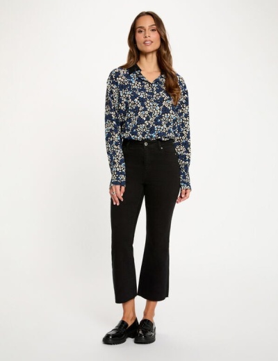 Mulher com camisa floral azul e calças pretas em fundo branco