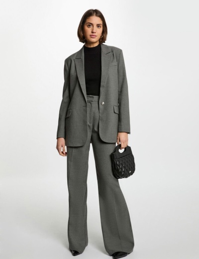 Mulher vestida com fato cinza formal e t-shirt preta, segurando bolsa preta acolchoada