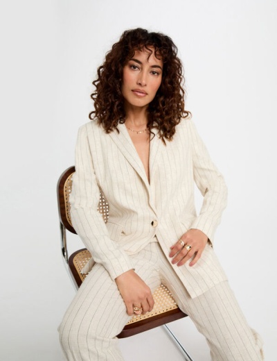 Conjunto feminino creme com riscas verticais, blazer e calças, sentado numa cadeira de madeira com palhinha.