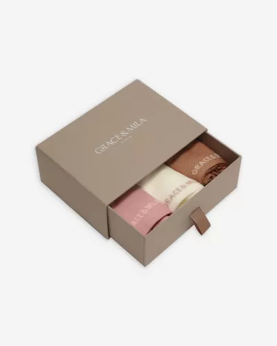 Caixa cinza com três meias rosa, branco e castanho dentro, texto GRACE + MILA HARLEM na tampa