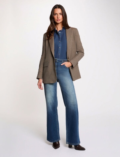 Mulher com blazer castanho, camisa denim e jeans azul em fundo branco