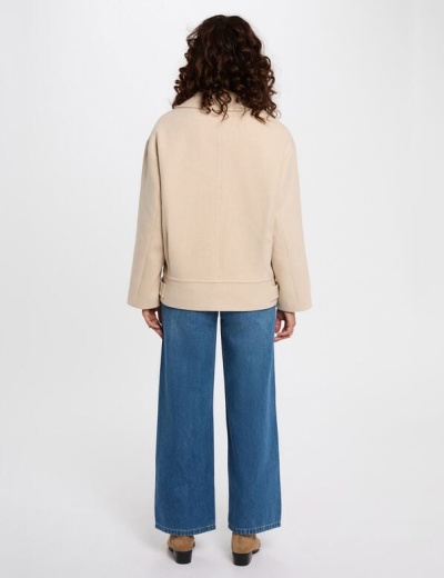 Vista traseira de casaco bege com calças de ganga azuis e sapatos castanhos.