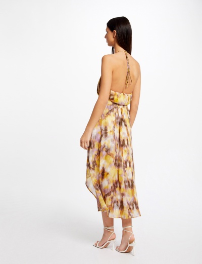 Mulher de costas a usar vestido midi estampado e sandálias de salto branco.
