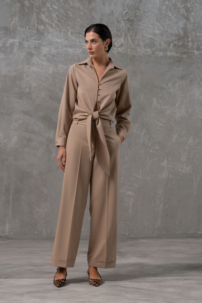 Mulher usando macacão bege com cinto e sapatos de salto animal print em fundo cinza.