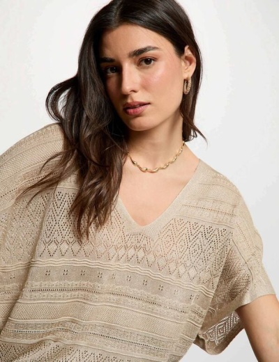 Mulher com blusa bege de malha rendada e joias douradas