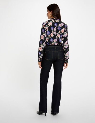 Mulher de costas a usar camisa preta floreada e calças de ganga pretas com costura amarela.