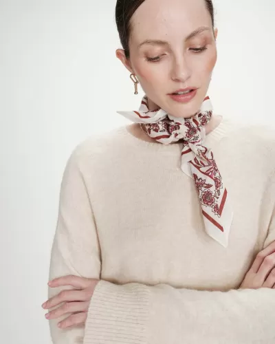 Mulher com lenço floral vermelho e rosa amarrado ao pescoço e camisola bege de malha