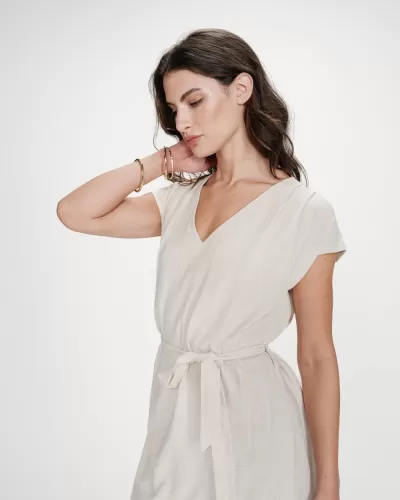 Vestido bege claro com cinto e decote em V usado por modelo com pulseiras douradas