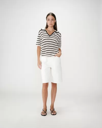 Mulher com camisola riscada, calções brancos e sandálias pretas em fundo branco