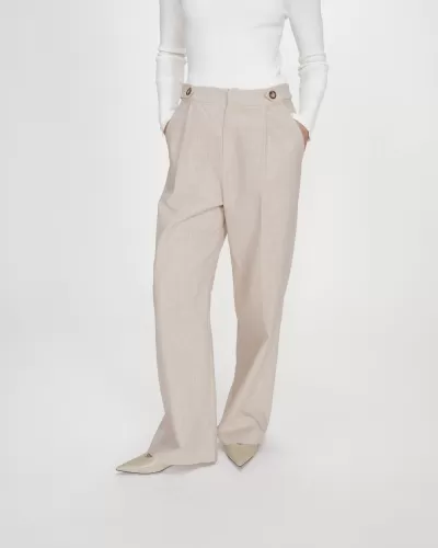 Calças largas bege com botões no cós, usadas com blusa branca e sapatos bege