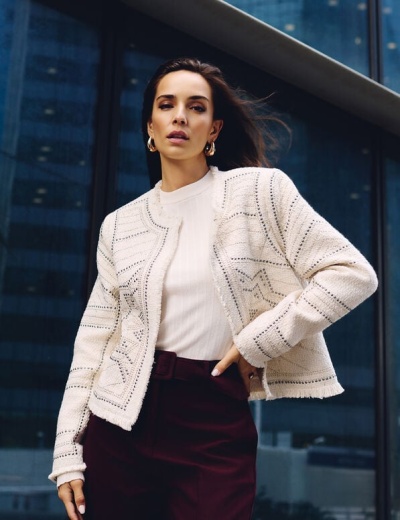 Mulher a usar casaco branco de malha com padrão de estrelas e calças bordô em cenário urbano