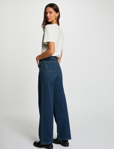 Mulher vista de costas com calças de ganga azul escuro largas e camisola branca